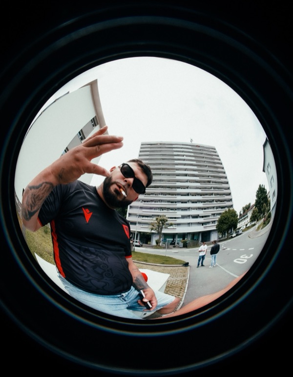 GABU mit Sonnenbrille grüsst in die Kamera, Fischauge vor Hochhaus