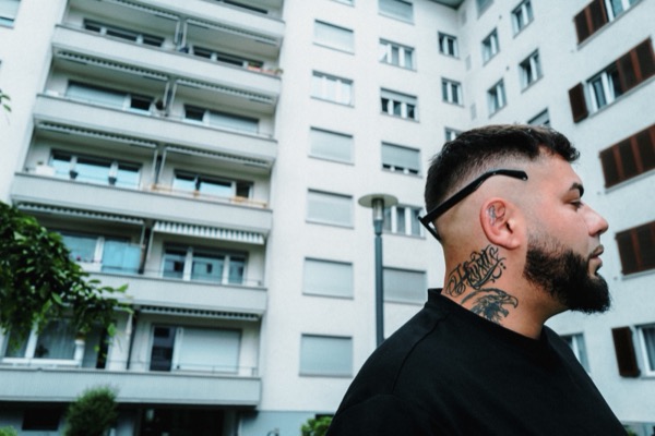 GABU im Profil mit Halstattoo vor einem Wohnblock
