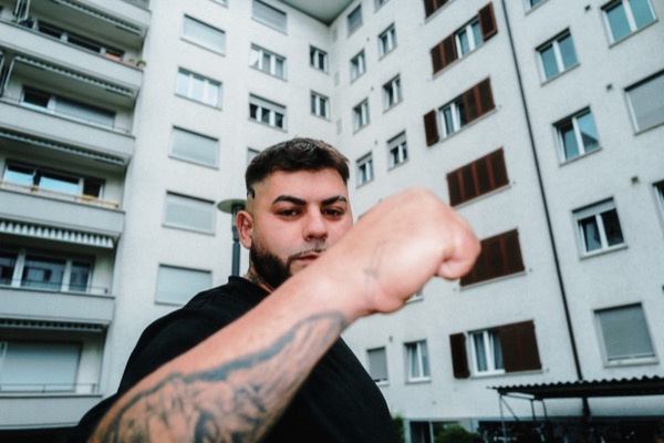 GABU streckt die Faust zur Kamera, Wohnblock im Hintergrund