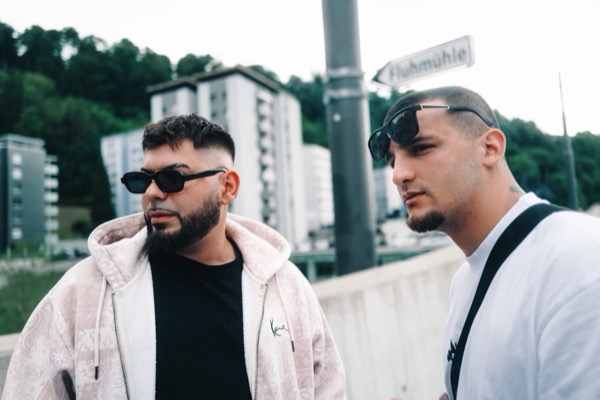 GABU mit Sonnenbrille und Begleiter vor Hochhäusern